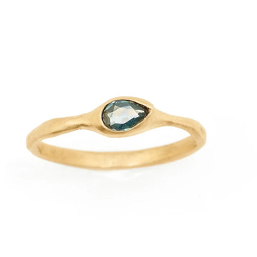 Montana Sapphire teal blue pear set horizontally on a simple textured yellow gold band