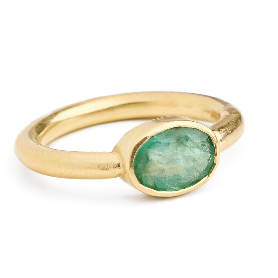 Oval faceted pale emerald ring set east -west in a round 18kt gold bezel ring. 